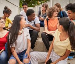 Multi-ethnic group of happy students on a break. Young people laugh sitting on the stairs of the high school.