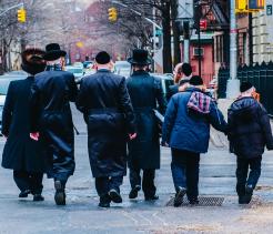 Men and boys in traditional Orthodox Jewish attire walking together through an urban neighborhood.