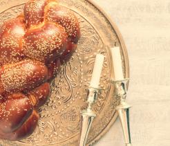 Braided challah bread on a decorative plate beside two Shabbat candles.