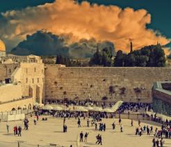 Western Wall plaza in Jerusalem with worshippers gathered beneath dramatic clouds.