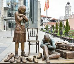 Bronze memorial sculpture depicting displaced children with worn shoes and suitcases in an urban plaza, evoking Holocaust-era displacement and loss.
