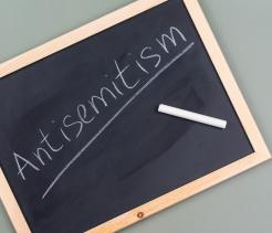 Chalkboard with wooden frame displaying the word "Antisemitism" written in white chalk, with a piece of chalk resting on the board's surface.