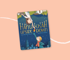 Cover of the children’s book Hanukkah Upside Down, illustrated with two children reaching toward each other around a spinning dreidel, with a city skyline in the background.