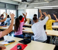 Group of high school students raising hands in classroom