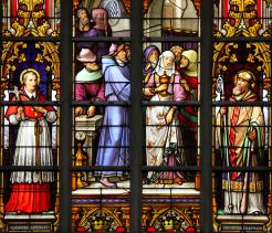 Stained glass window depicting a medieval Christian religious scene with clergy and figures gathered in a ritual setting, used to illustrate historical Christian imagery and its role in European religious culture.