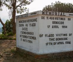 A white concrete memorial monument with black lettering commemorating 11,400 victims of the genocide on April 17, 1994. The text appears in multiple languages, including French and English, and the monument stands outdoors on a brick base surrounded by trees and vegetation.