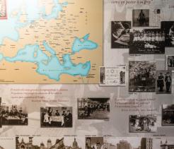 A museum-style display featuring a large map of Europe surrounded by historical black-and-white photographs, documents, and captions, many related to Jewish communities and history, with Spanish quotations from religious texts printed across the background.