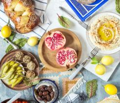 Composition of israel and middle eastern food: ritual goblet of wine, challah, pita bread, hummus, falafel, shakshuka, pomegranate and lemons on a rustic table