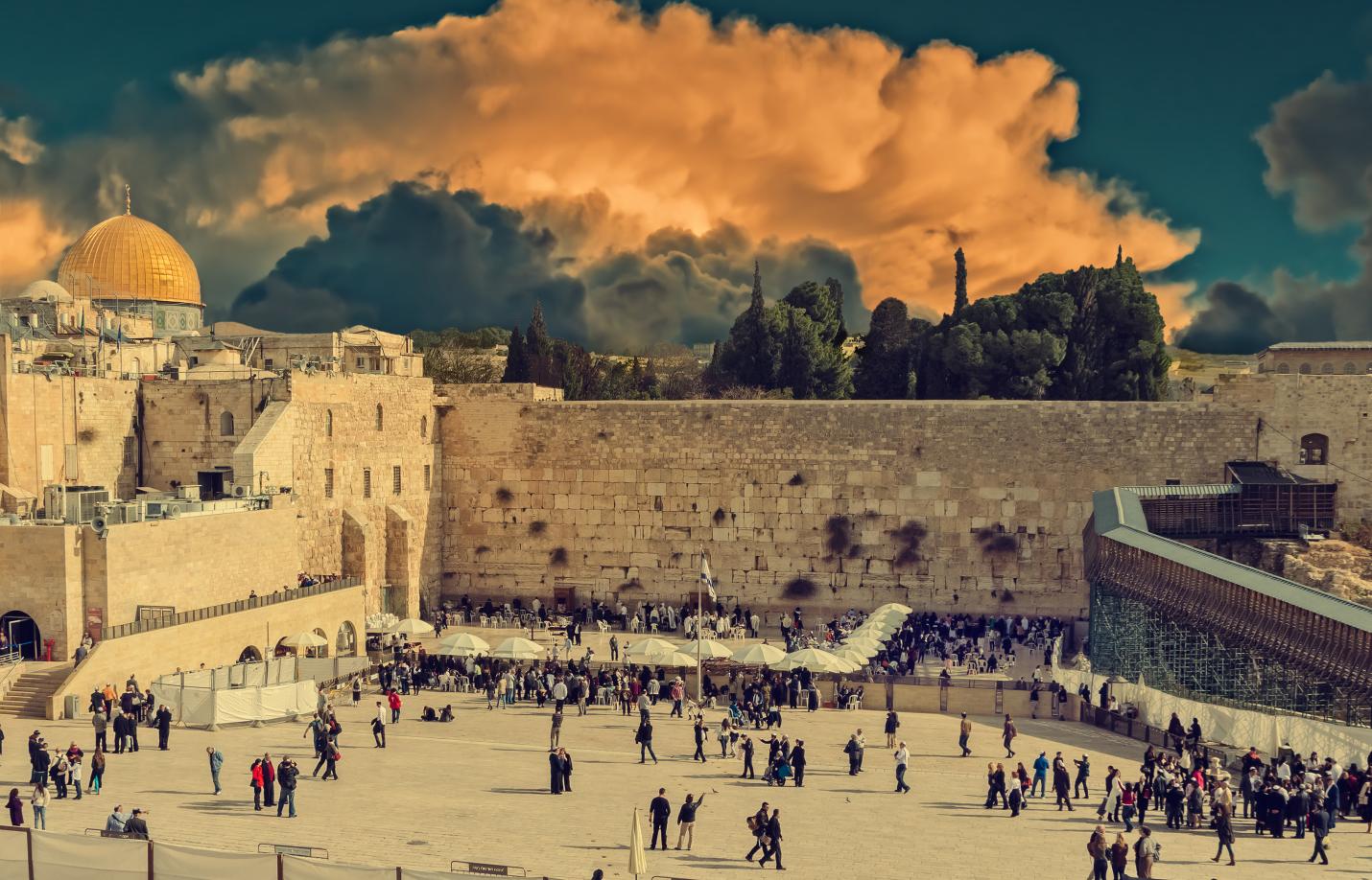 Western Wall plaza in Jerusalem with worshippers gathered beneath dramatic clouds.
