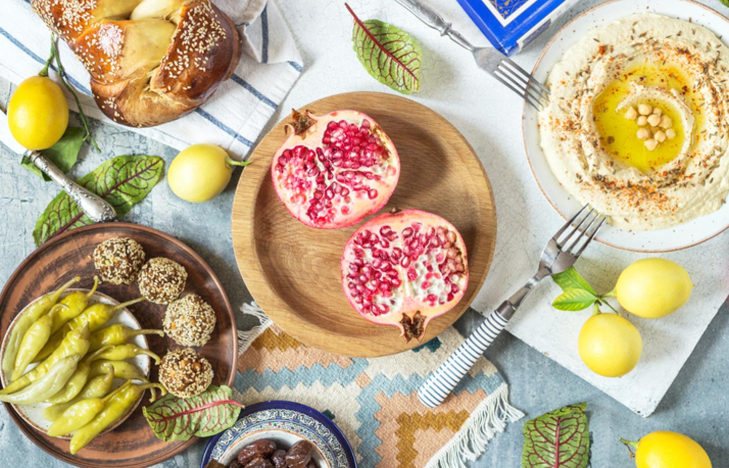 Composition of israel and middle eastern food: ritual goblet of wine, challah, pita bread, hummus, falafel, shakshuka, pomegranate and lemons on a rustic table