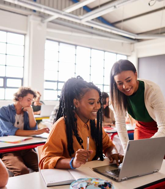 Teacher and students looking at work on laptop and smiling